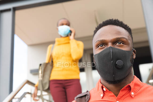 Serious african american business creative colleagues wearing face masks walking downstairs. independent creative business people at a modern office at coronavirus covid 19 pandemic. — Stock Photo