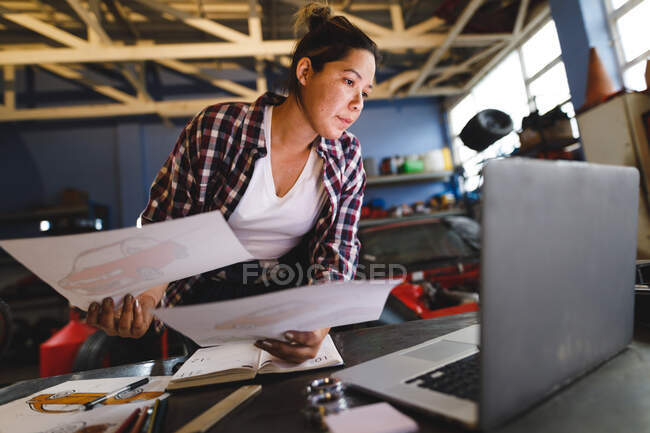 Змішана гонка жіночий автомеханік сидить за столом, роблячи паперові роботи в майстерні. незалежний власник бізнесу в гаражі з обслуговування автомобілів . — стокове фото