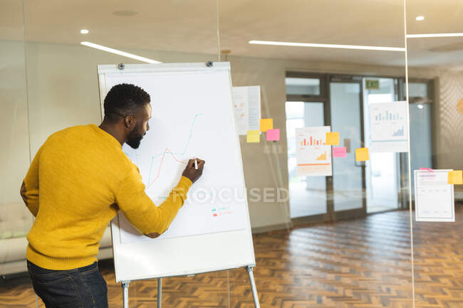 Negocio masculino afroamericano serio creativo usando pizarra blanca, haciendo la presentación. empresarios creativos independientes que trabajan en una oficina moderna. - foto de stock