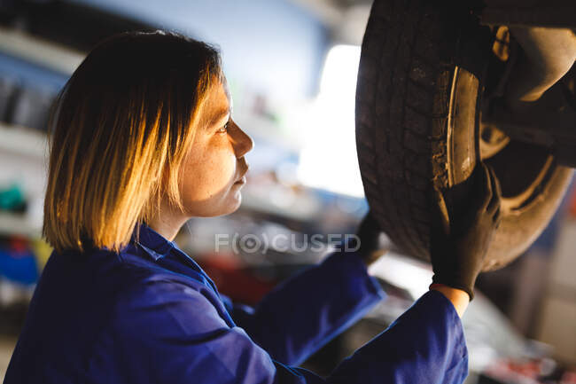 Mixed race female car mechanic wearing overalls, unbolting wheel of car. independent business owner at car servicing garage. — Stock Photo