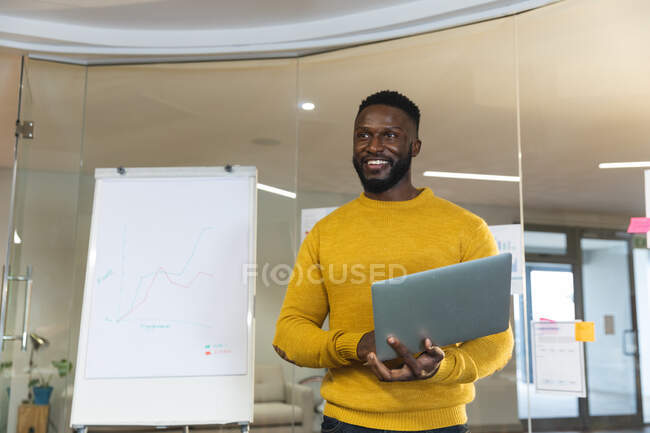 Sorridente afroamericano uomo d'affari creativo che tiene il computer portatile, facendo presentazione. uomini d'affari creativi indipendenti che lavorano in un ufficio moderno. — Foto stock