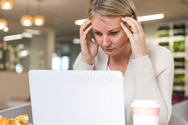 Negócio feminino caucasiano estressado criativo usando laptop no refeitório do local de trabalho. empresários criativos independentes que trabalham em um escritório moderno. — Fotografia de Stock