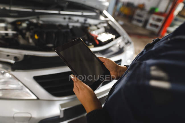 Close-up de mãos de mestiço feminino carro mecânico vestindo macacão, usando tablet. proprietário de empresa independente na garagem de manutenção de carro. — Fotografia de Stock