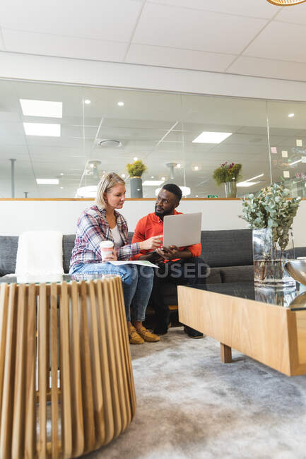 Serious diverse female and male colleagues sitting on sofa at workplace lounge area and talking. independent creative business people at a modern office. — Stock Photo