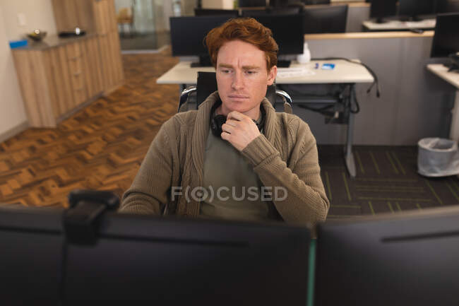 Белый мужчина креативный на работе, сидит за столом, за компьютером. работа в творческом бизнесе в современном офисе. — стоковое фото