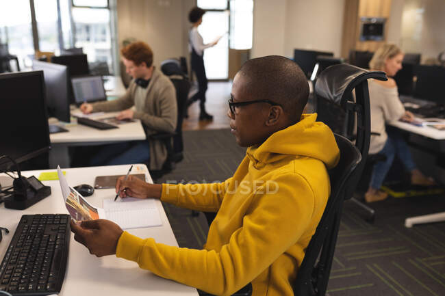 Diverse männliche und weibliche Kollegen bei der Arbeit, am Schreibtisch, am Computer, Notizen machen. Arbeit im kreativen Geschäft in einem modernen Büro. — Stockfoto