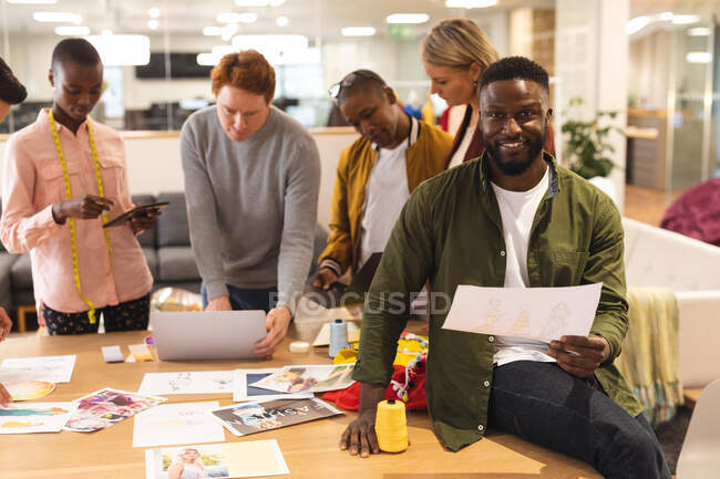 Lächelnd arbeiten diverse männliche und weibliche Kollegen zusammen und diskutieren in lockerer Runde. Arbeit im kreativen Geschäft in einem modernen Büro. — Stockfoto