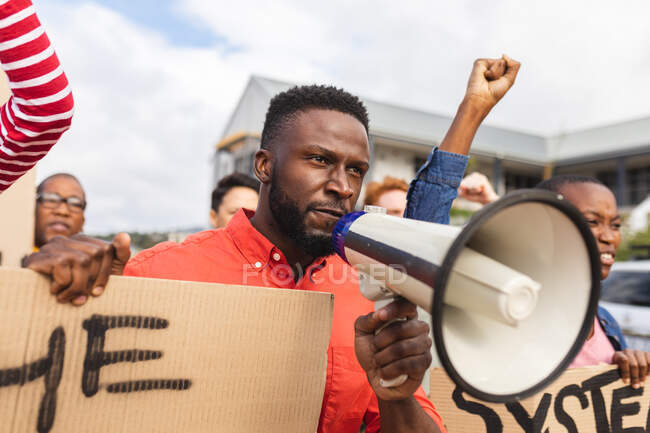 Hombre afroamericano usando megáfono y sosteniendo pancarta en una marcha de protesta. manifestantes por la igualdad de derechos y justicia en marcha. - foto de stock