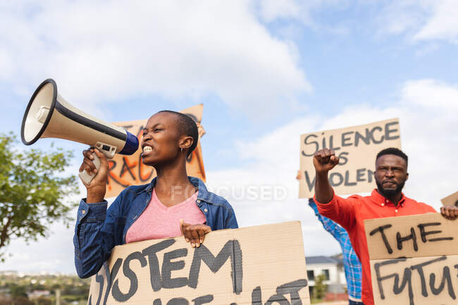 Mujer afroamericana usando megáfono y sosteniendo pancarta en una marcha de protesta. manifestantes por la igualdad de derechos y justicia en marcha. - foto de stock