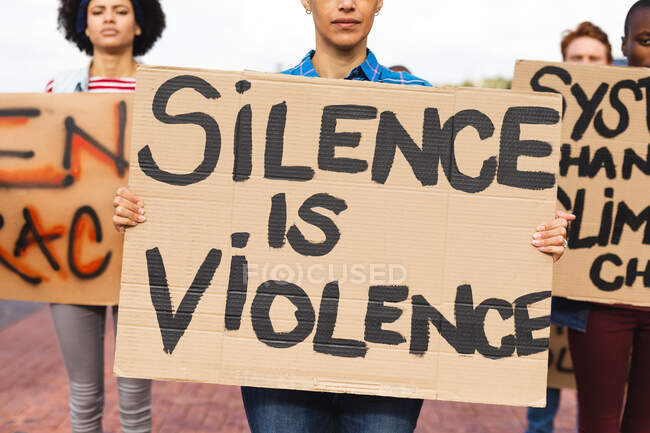 Frau mit gemischter Rasse hält Plakat hoch, auf dem steht: Schweigen ist Gewalt bei Protestmarsch. Demonstranten für gleiche Rechte und Gerechtigkeit auf Demonstrationszug. — Stockfoto