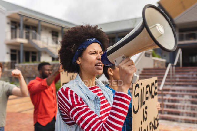 Mujer de raza mixta usando megáfono y sosteniendo pancarta en una marcha de protesta. manifestantes por la igualdad de derechos y justicia en marcha. - foto de stock