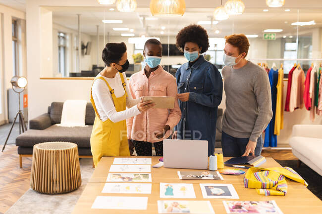 Diverse male and female colleagues wearing face masks, working together at desk using tablet. working in creative business at a modern office during coronavirus pandemic. — Stock Photo