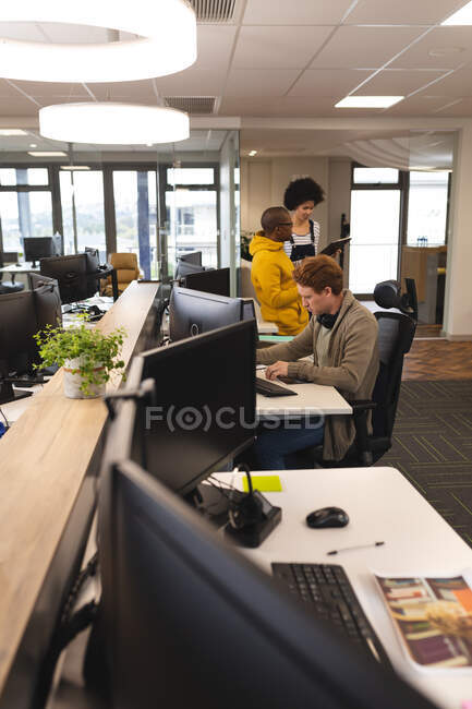 Diversos colegas masculinos y femeninos en el trabajo, sentados en escritorios, usando computadoras. trabajar en un negocio creativo en una oficina moderna. - foto de stock