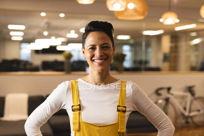 Retrato de raza mixta sonriente femenina creativa mirando a la cámara. trabajar en un negocio creativo en una oficina moderna. - foto de stock