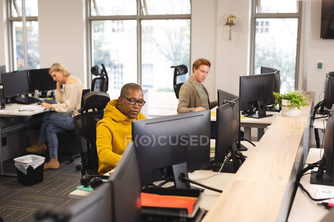 Diversos colegas masculinos y femeninos en el trabajo, sentados en escritorios, usando computadoras. trabajar en un negocio creativo en una oficina moderna. - foto de stock