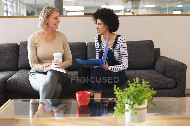 Lächelnd arbeiten diverse Kolleginnen im Lounge-Bereich des Arbeitsplatzes zusammen. Arbeit im kreativen Geschäft in einem modernen Büro. — Stockfoto