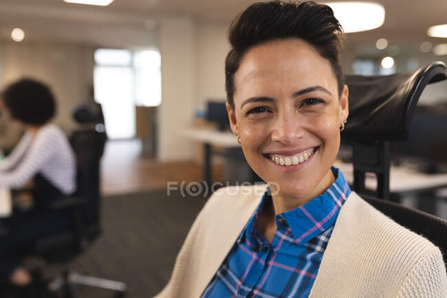 Портрет улыбающейся смешанной расы женщины творческой на работе, сидящей за столом, смотрящей в камеру. работа в творческом бизнесе в современном офисе. — стоковое фото