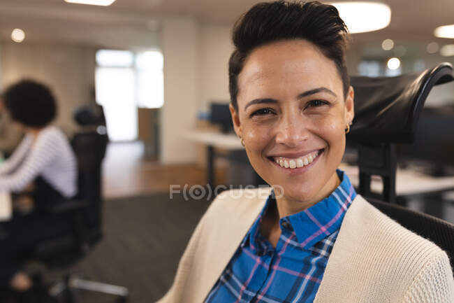 Portrait de femme souriante métissée créative au travail, assise au bureau, regardant vers la caméra. travailler dans une entreprise créative dans un bureau moderne. — Photo de stock