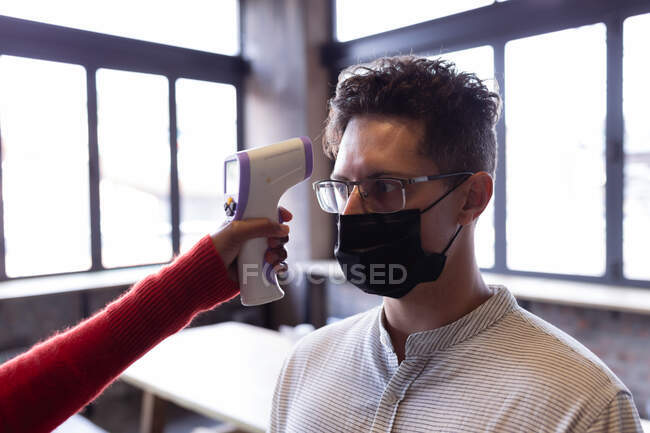 Кавказький чоловік, одягнений в маску обличчя, вимірює температуру на винокурні джину. Незалежний винокурний бізнес під час пандемії коварідів-19. — стокове фото