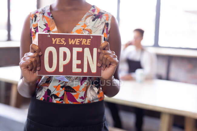 Mid section of african american woman holding we are open signboard at gin distillery. independent craft gin distillery business concept — Stock Photo