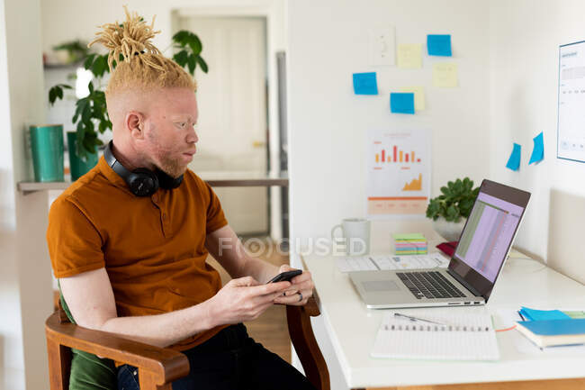 Albino african american man with dreadlocks working from home and using smartphone laptop. remote working using technology at home. — Stock Photo