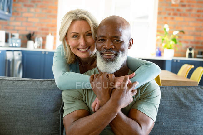 Porträt eines glücklichen Seniorenpaares im Wohnzimmer, das auf dem Sofa sitzt, sich umarmt und lächelt. Lebensstil im Ruhestand, Zeit zu Hause verbringen. — Stockfoto