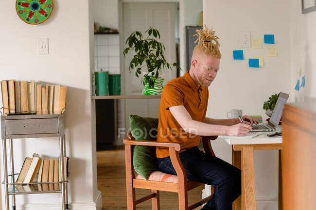 Albino african american man with dreadlocks working from home and using laptop. remote working using technology at home. — Stock Photo