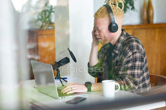 Albino hombre afroamericano con rastas trabajando desde casa y haciendo podcast. trabajo remoto utilizando tecnología en el hogar. - foto de stock