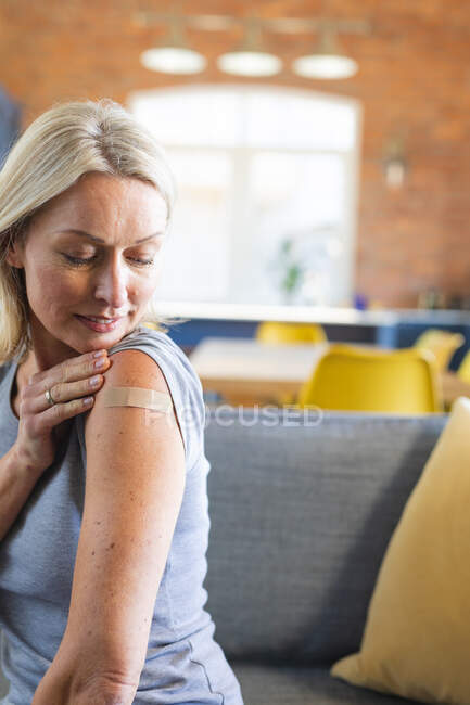 Happy senior caucasian woman in living room with bandage on her arm. senior health and lifestyle during covid 19 pandemic. — Stock Photo