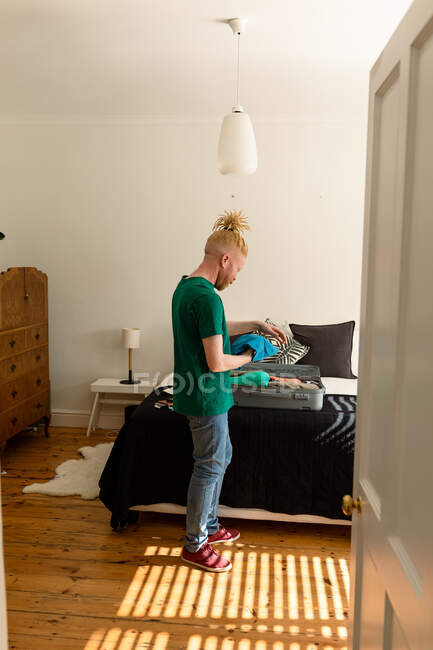 Afroamericano albino uomo con serrature terrore imballaggio valigia in camera da letto. vacanza e preparazione di viaggio. — Foto stock