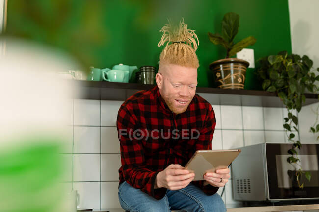 Happy albino african american man with dreadlocks working from home and using tablet. remote working using technology at home. — Stock Photo