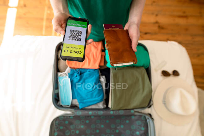 Man packing and holding smartphone with covid 19 vaccine passport. holiday and travel preparation during covid 19 pandemic. — Stock Photo