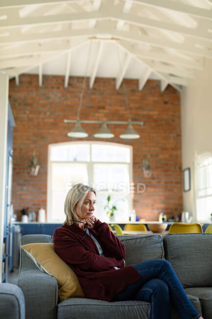 Nachdenkliche Seniorin im Wohnzimmer, die auf dem Sofa sitzt und nachdenkt. Lebensstil im Ruhestand, Zeit zu Hause verbringen. — Stockfoto