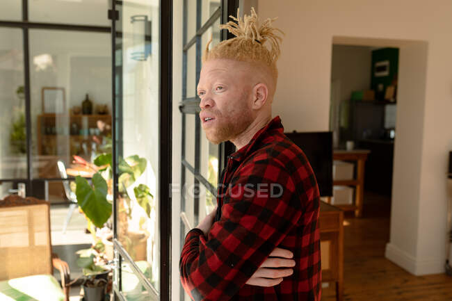 Продуманий альбіно-афроамериканський чоловік з дредлоками, який дивиться у вікно. дистанційна робота з використанням технології вдома . — стокове фото