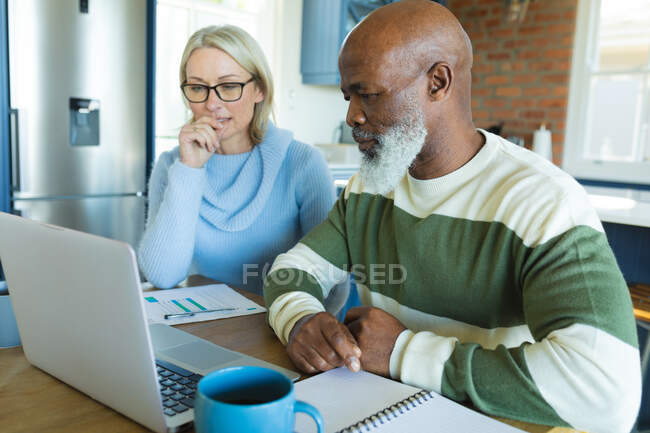 Пожилая пара сидела на кухне за столом, используя ноутбук. уход на пенсию образ жизни, дома с технологиями. — стоковое фото
