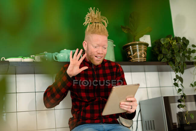 Glücklicher afrikanischer Albino-Mann mit Dreadlocks, der Videotelefonate führt und ein Tablet benutzt. Fernbedienung mit Technologie zu Hause. — Stockfoto