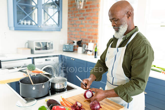Feliz hombre afroamericano mayor en la cocina con delantal de cocina. estilo de vida saludable y activo de jubilación en el hogar. - foto de stock