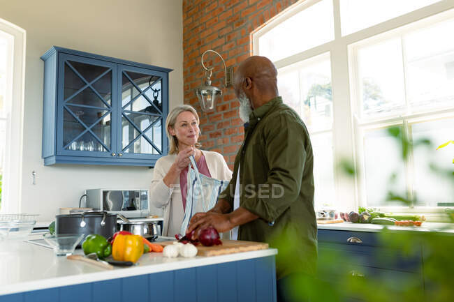Heureux couple diversifié senior dans la cuisine cuisine ensemble, portant tablier. mode de vie sain et actif à la retraite à la maison. — Photo de stock
