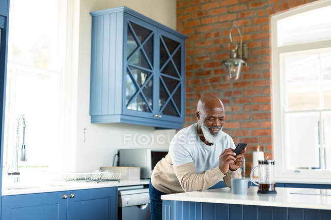 Homem americano africano sênior feliz na cozinha usando smartphone. estilo de vida de aposentadoria, em casa com tecnologia. — Fotografia de Stock