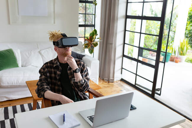 Nachdenklicher afrikanisch-amerikanischer Albino-Mann mit Dreadlocks, der von zu Hause aus arbeitet und VR-Headsets benutzt. Fernbedienung mit Technologie zu Hause. — Stockfoto