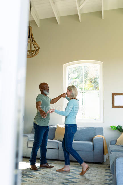Happy senior diverse couple in living room dancing together. retirement lifestyle, spending time at home. — Stock Photo