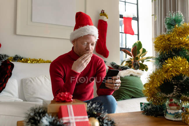 Albino uomo afroamericano con cappello da Babbo Natale che fa videochiamate con decorazioni natalizie. Natale, festività e tecnologia della comunicazione festività e tecnologia della comunicazione. — Foto stock