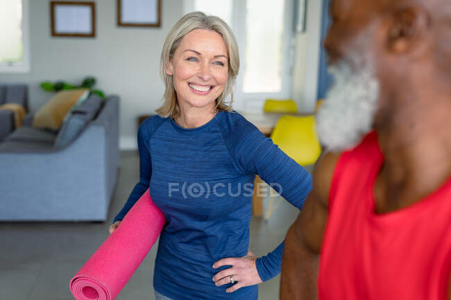 Glückliches älteres Paar in Turnkleidung, das gemeinsam Yoga praktiziert, Matten hält und lächelt. gesunder, aktiver Lebensstil im Ruhestand zu Hause. — Stockfoto