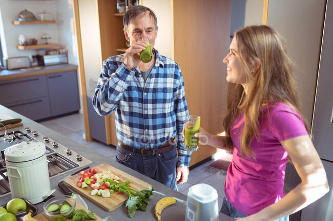 Caucasian grandfather and granddaughter drinking smoothie in kitchen. active and healthy retirement lifestyle at home. — Stock Photo