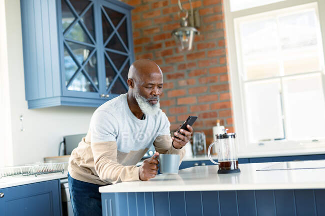 Happy senior african american man in kitchen using smartphone. retirement lifestyle, at home with technology. — Stock Photo