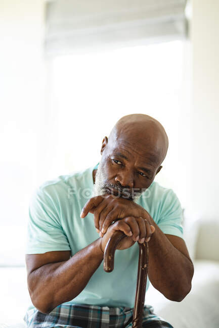 Pensativo hombre afroamericano mayor en el dormitorio sosteniendo bastón. estilo de vida de jubilación, pasar tiempo en casa. - foto de stock