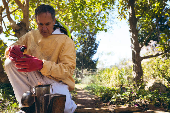 Uomo anziano caucasico in uniforme da apicoltore che prepara il fumo per calmare le api. apicoltura, apiario e miele concetto di produzione. — Foto stock