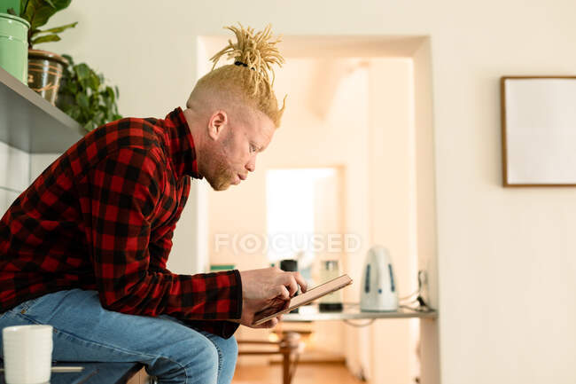 Albino african american man with dreadlocks working from home and using tablet. remote working using technology at home. — Stock Photo