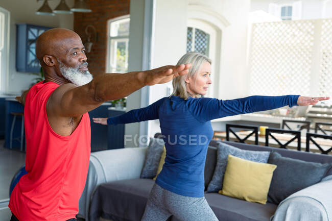 Счастливая старшая разнообразная пара в спортивной одежде практикующих йогу вместе, растяжения. здоровый, активный образ жизни на дому. — стоковое фото
