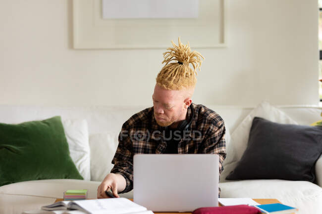 Homme afro-américain albinos avec dreadlocks travailler de la maison et en utilisant un ordinateur portable. télétravail utilisant la technologie à la maison. — Photo de stock